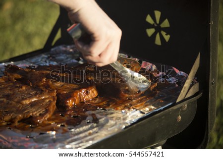 Someone with tongs turning a ribeye steak on a grill