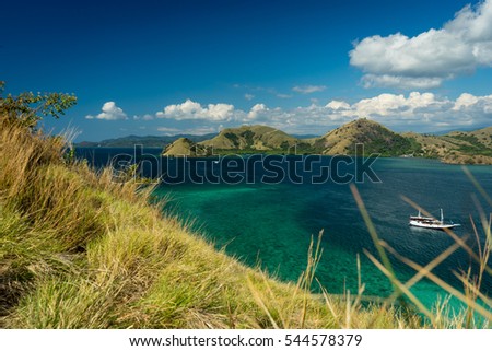 Coral Bay. Viewpoint over Komodo National Park, Flores, Indonesia. Dry grass in the foreground, turquoise coral reef in and one ship the water, iconic mountains in the background.