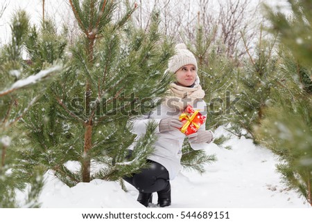 The happy young girl holds in hand a box with a New Year's gift, among trees, fir-trees and pines