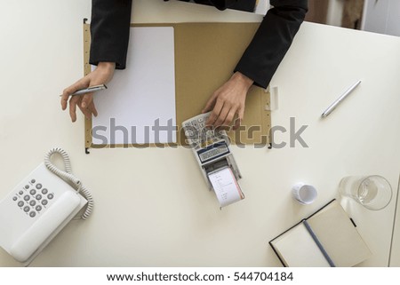 Overhead view of businessperson using a calculator on a desk with blank paper.