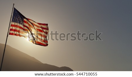 Back-lit American flag flying on pole with copy space.  Royalty-Free Stock Photo #544710055