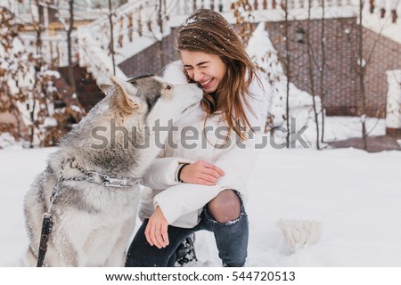 Portrait cute lovely moments of husky dog kissing fashionable young woman outdoor in snow. Cheerful mood, winter holidays, snow time, real friendship, animals love
