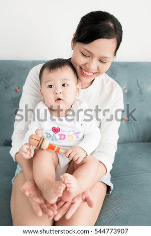 Mother and baby daughter plays, hugging, kissing at home on the couch