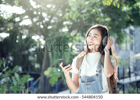 Young traveler hipster wear headphone listening to music through smartphone standing outdoors on nature background.