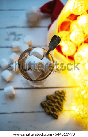 Cup of  cocoa, fir-tree gingerbread, marshmallows, hat of Santa Claus and lights on white wooden background. Top view
