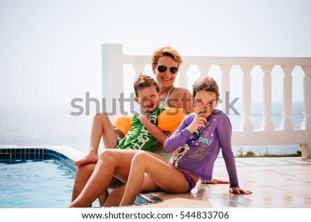 Mother, daughter and son are sitting pool side at an exotic location such as a villa or a hotel.