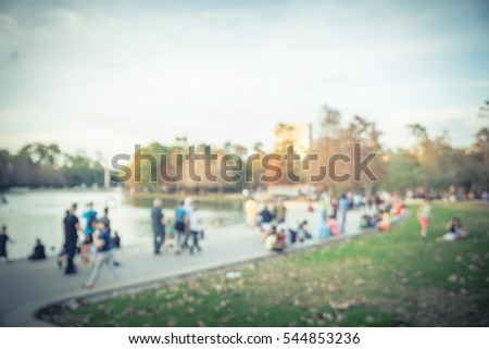 Blurred image kids running on grass lawn and people sitting and enjoying fresh air on stairs toward the lake at Houston, Texas, US. Defocused outdoor family activities near lake in city park at sunset