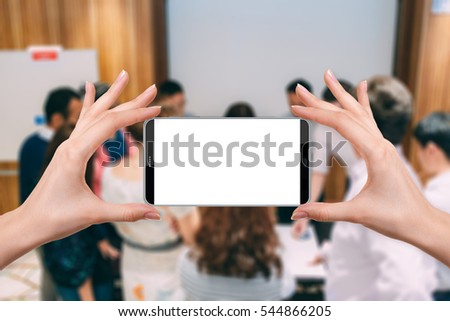 female holding a smartphone isolated blank screen with two hands onabstract blur background of closeup people in group meeting in convention hall, ready for snap a picture