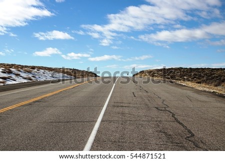 American road trip in Colorado with open blue sky, long road with nobody on road. White and yellow lines on road.