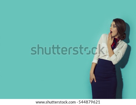 Young suprised woman looking left with her hand beside mouth. Shocked expression. Blue background  in studio Royalty-Free Stock Photo #544879621