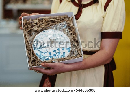 Woman holds round gingerbread with picture of blue flowers on it