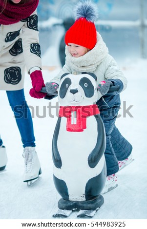 Little adorable girl learning to skate on ice rink outdoor