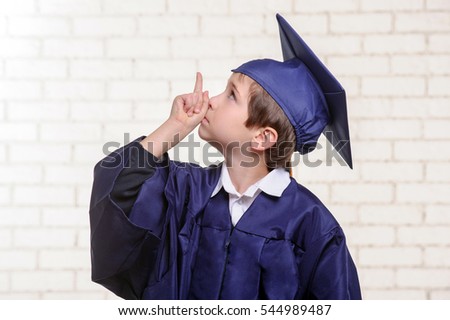 School boy in graduation dress points up with his finger.