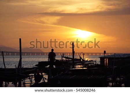 Silhouette of a man enjoying sunrise on a fishing pier/jetty with bridge connecting to an island on the background