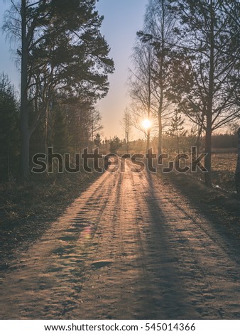 winter landscape of sunset over the country gravel road and forest - vintage color film look