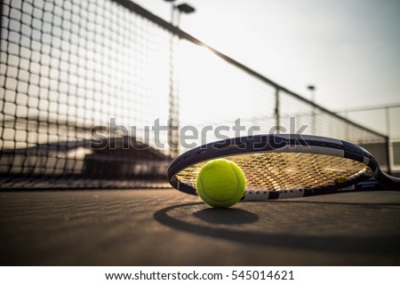 Tennis ball and racket on hard court under sunlight Royalty-Free Stock Photo #545014621