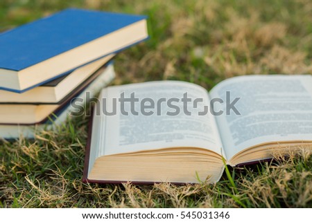 Open book on the grass with pile of closed books on grass background.