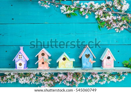 Blank wood sign with colorful birdhouses with butterfly on shelf by spring tree flowers on antique rustic teal blue wooden background; holiday background with painted copy space