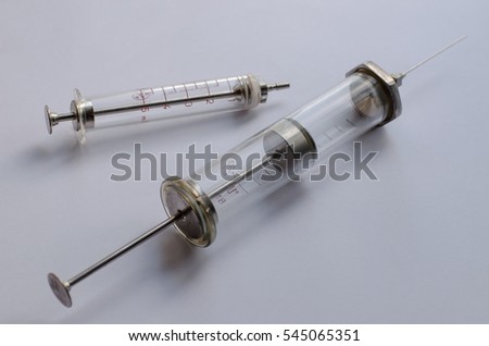 Two metal/glass reusable syringes against white background, first one has volume of 20 ml, another one has volume of 5 ml