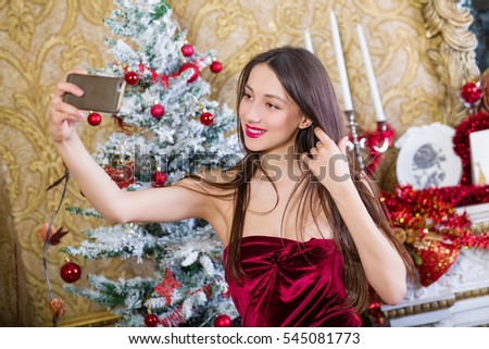 Young smiling woman makes selfie in room decorated to christmas holidays.