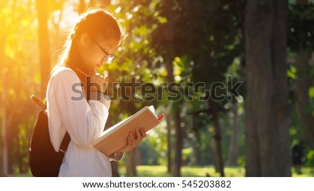 Asian student girl reading book in the park with sun shining background, people, learning, education and school concept