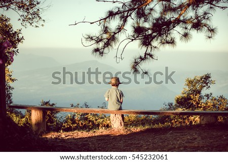 Silhouette of young boy sitting on sunset or sunrise. Confident teenage boy thinking on cliff stone. Hope. Sadness. Freedom.