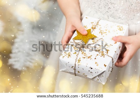Little girl's hands holding white gift box with gold star, New year present, Christmas bokeh lights