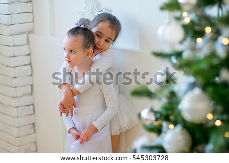 Two young ballet dancer hug near Christmas tree on the wooden floor and smile