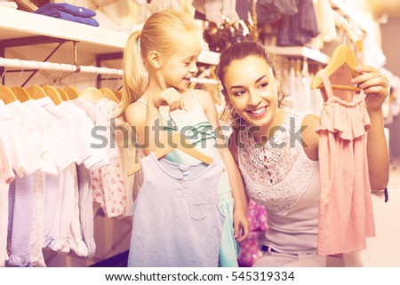 portrait of positive russian woman and girl shopping kids apparel in clothes store