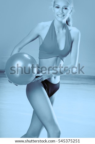 Young beautiful happy smiling blond woman in sportswear playing with red gym ball on sea beach. Black and white.