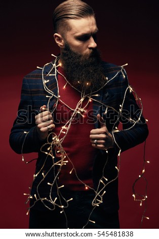 Portrait of serious handsome man with beard and christmas garland in studio 