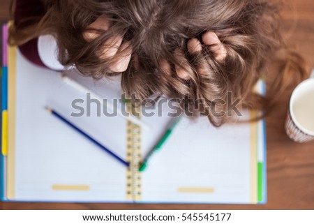 Beautiful cute little blond girl with glasses and purple dress working or drawing or coloring in the notebook. Frustration and pulling the hair. 