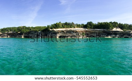 Striking panoramic view of white and grey cliffs in Pictured Rocks National Park with a waterfall and bright clear cold blue water