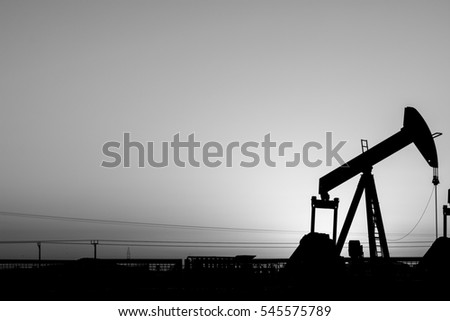 Silhouette of crude oil pump in the oil field against sunset - black and white