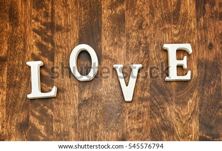 Word 'love' on wooden textured background. The letters are capitals and white in color. The background is a dark brown wood and its texture is clearly visible. No persons in image. 