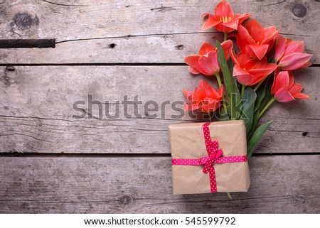 Bunch of coral tulips and wrapped box with present  on vintage  wooden background. Selective focus. Place for text. Flat lay.
