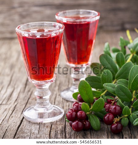 Sweet cranberry liqueur in two glasses on the background of ripe berries on a dark wooden background. selective Focus