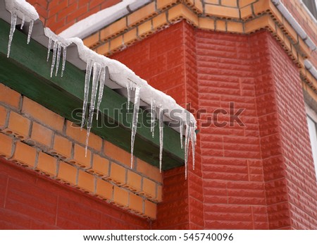 Many icicles hanging on the roof. Large and heavy icicles hanging from the roof of the building. Transparent icicles made from frozen snow melting. Royalty-Free Stock Photo #545740096