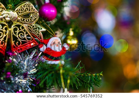 Father Christmas decoration hanging from a Christmas tree against bokeh background.