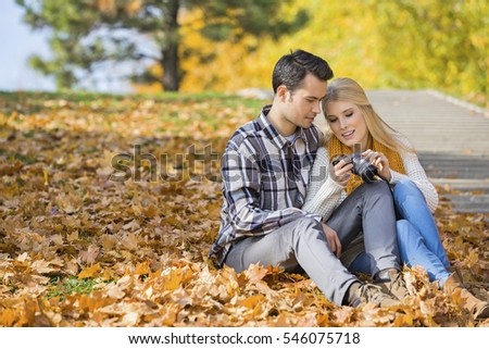 Couple looking at pictures on digital camera in park during autumn