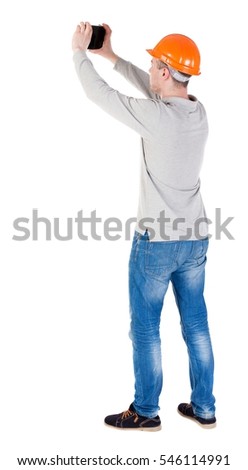 Backview of an engineer in construction helmet stands and enjoys tablet or using a mobile phone. Standing young guy. Rear view  collection.  backside view of person.  Isolated over white background.