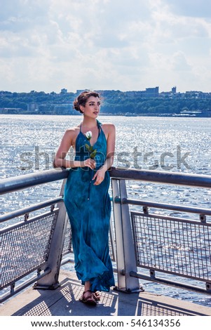 Woman Missing You. A pretty girl wearing long blue dress, sandals, holding white rose, standing by Hudson River in New York in hot summer, crossing New Jersey, waiting you. Color filtered effect.