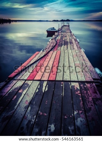 A small boat sits silently beside a weathered dock. Royalty-Free Stock Photo #546163561