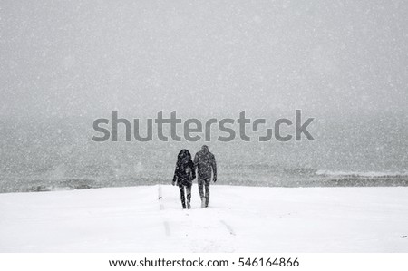 Couple holding hands walking toward Lake Michigan on a snowy day during a winter blizzard 