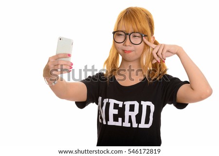 Young cute Asian nerd woman taking selfie with mobile phone and thinking isolated against white background