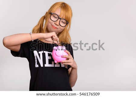 Young cute Asian nerd woman putting coin in piggy bank isolated against white background