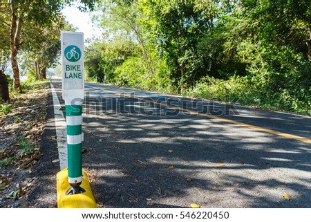 focus bike lane sign pole with green tree and way for bicycle in background