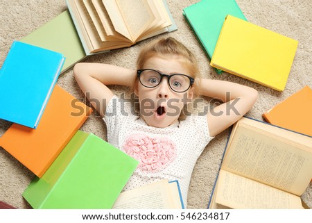 Emotional little girl lying on carpet among books