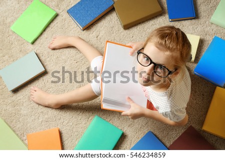 Cute little girl reading book while sitting on carpet