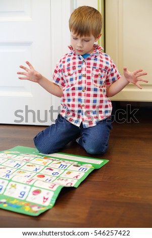 Little boy in jeans plays with interactive alphabet on floor in room 